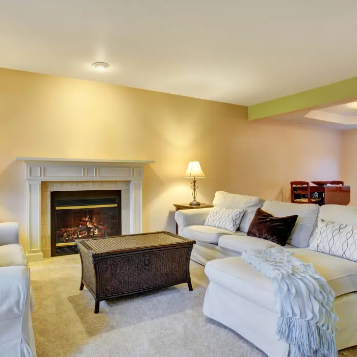 A cozy living room bathed in warm light, featuring a fireplace that invites relaxation. Plush sofas adorned with soft pillows create a welcoming atmosphere, while a coffee table centers the space, perfect for gatherings or quiet evenings at home.