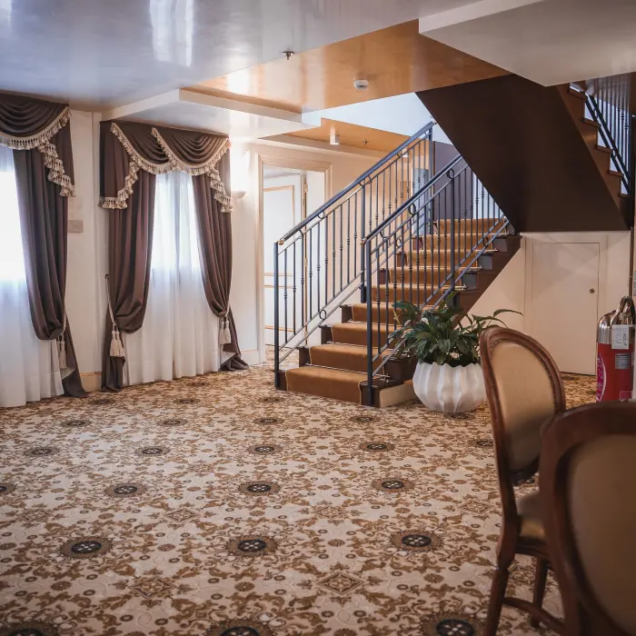 Empty living room with staircase and carpeted floor in neutral color scheme and minimalist design.